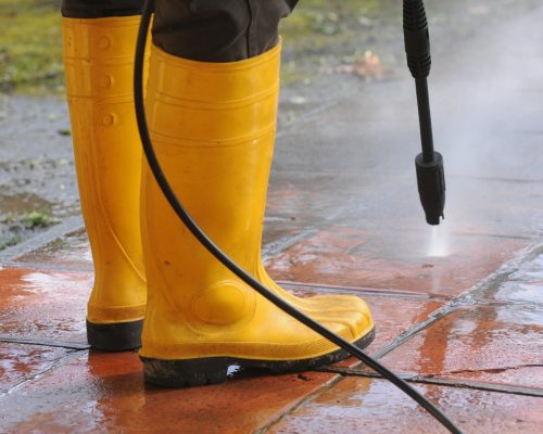person-wearing-yellow-rubber-boots-with-high-pressure-water-nozzle-cleaning-dirt-tiles